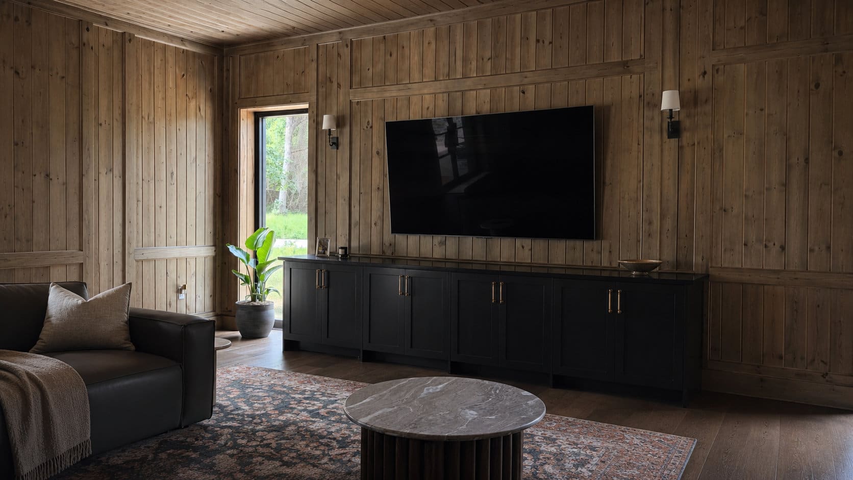Warm wood-paneled living space with custom black media built-in by Silver Branch Millwork